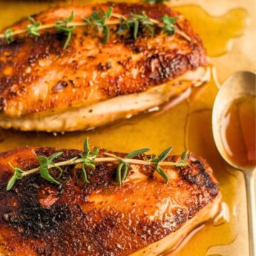 crispy hot honey chicken breast on a parchment paper garnished with thyme and a spoon of honey beside it