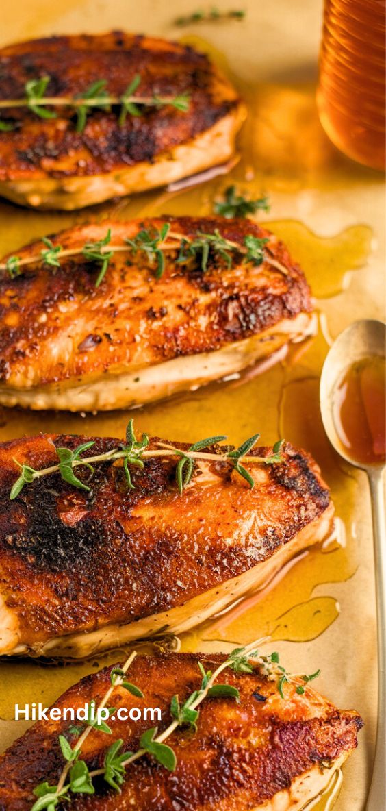 crispy hot honey chicken breast on a parchment paper garnished with thyme and a spoon of honey beside it