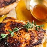 crispy hot honey chicken breast on a parchment paper garnished with thyme and a spoon of honey beside it